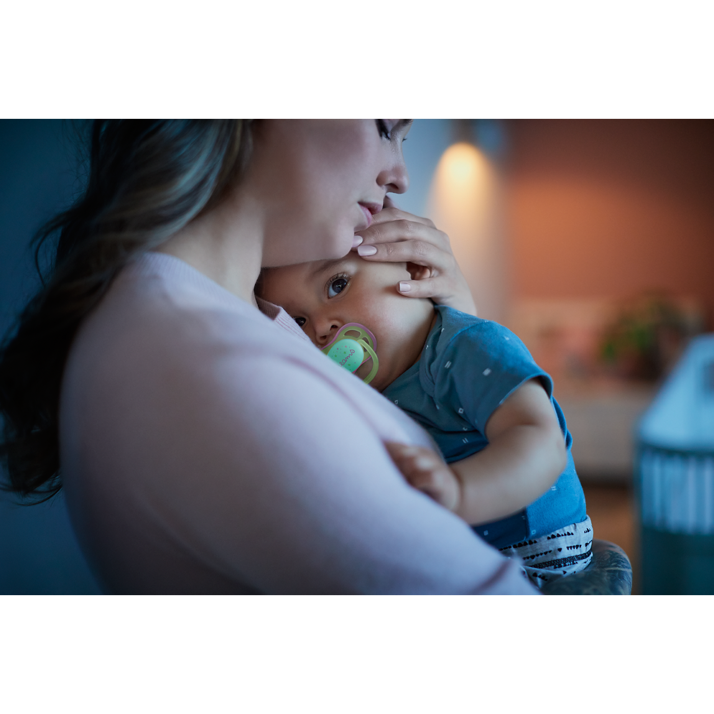 Woman holding a baby with a pacifier in a cozy indoor setting