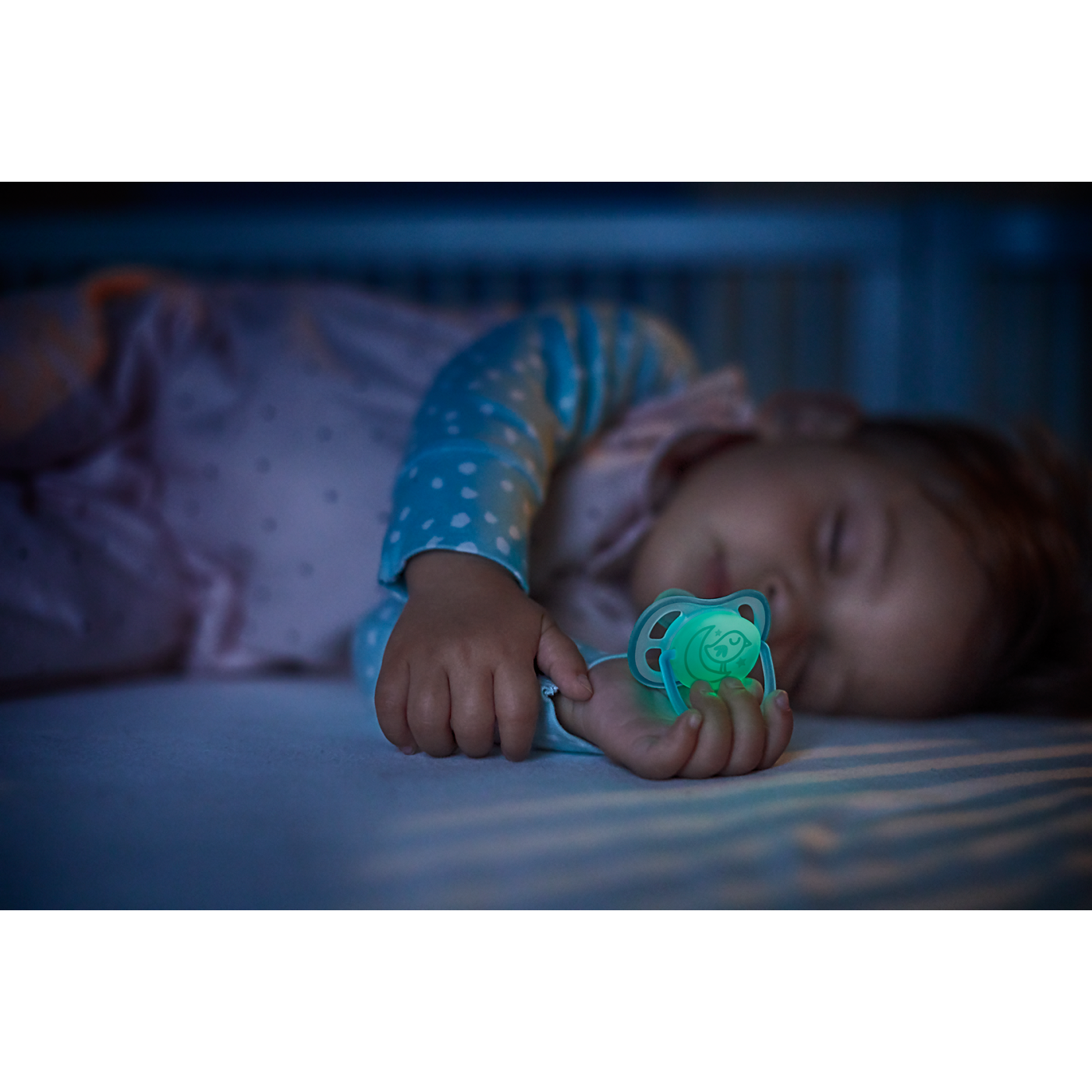 Baby sleeping in a crib with a green pacifier