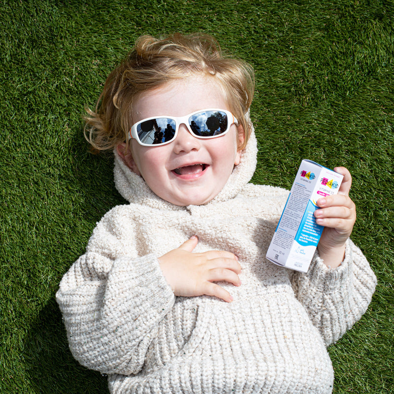 Child wearing sunglasses and holding a PEDIAKID product package on grass