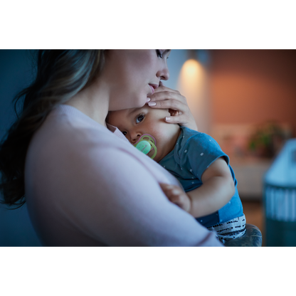 Woman holding a baby with a pacifier in a cozy indoor setting