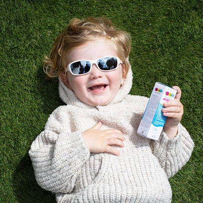Child wearing sunglasses and holding a PEDIAKID product package on grass